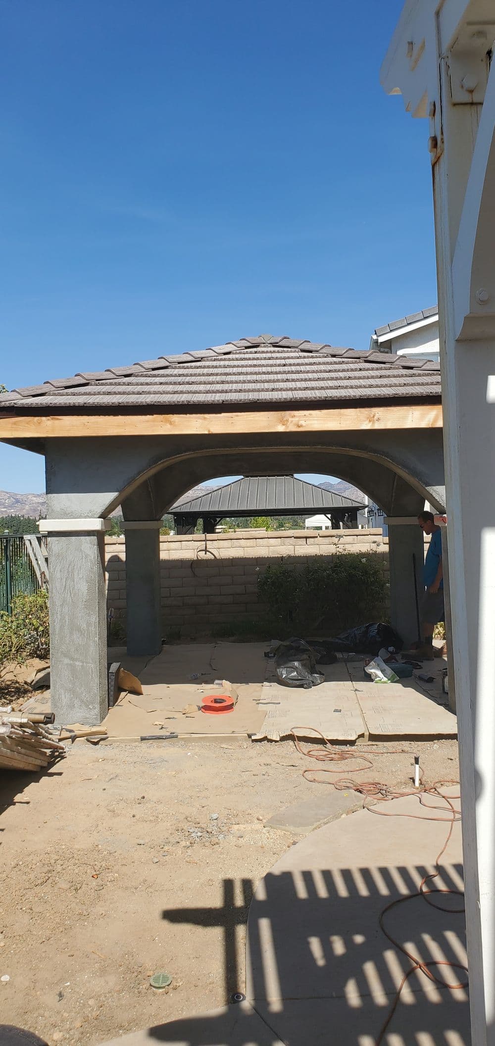 Construction of a gazebo with stone columns and a tiled roof in a backyard setting.