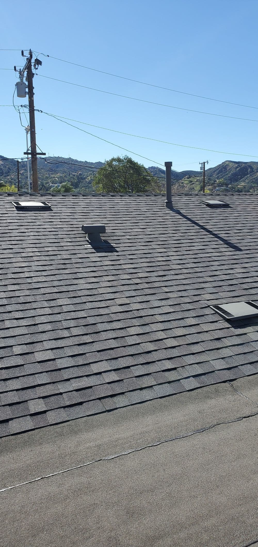 Roof with shingles and vent, overlooking distant mountains under a clear blue sky.