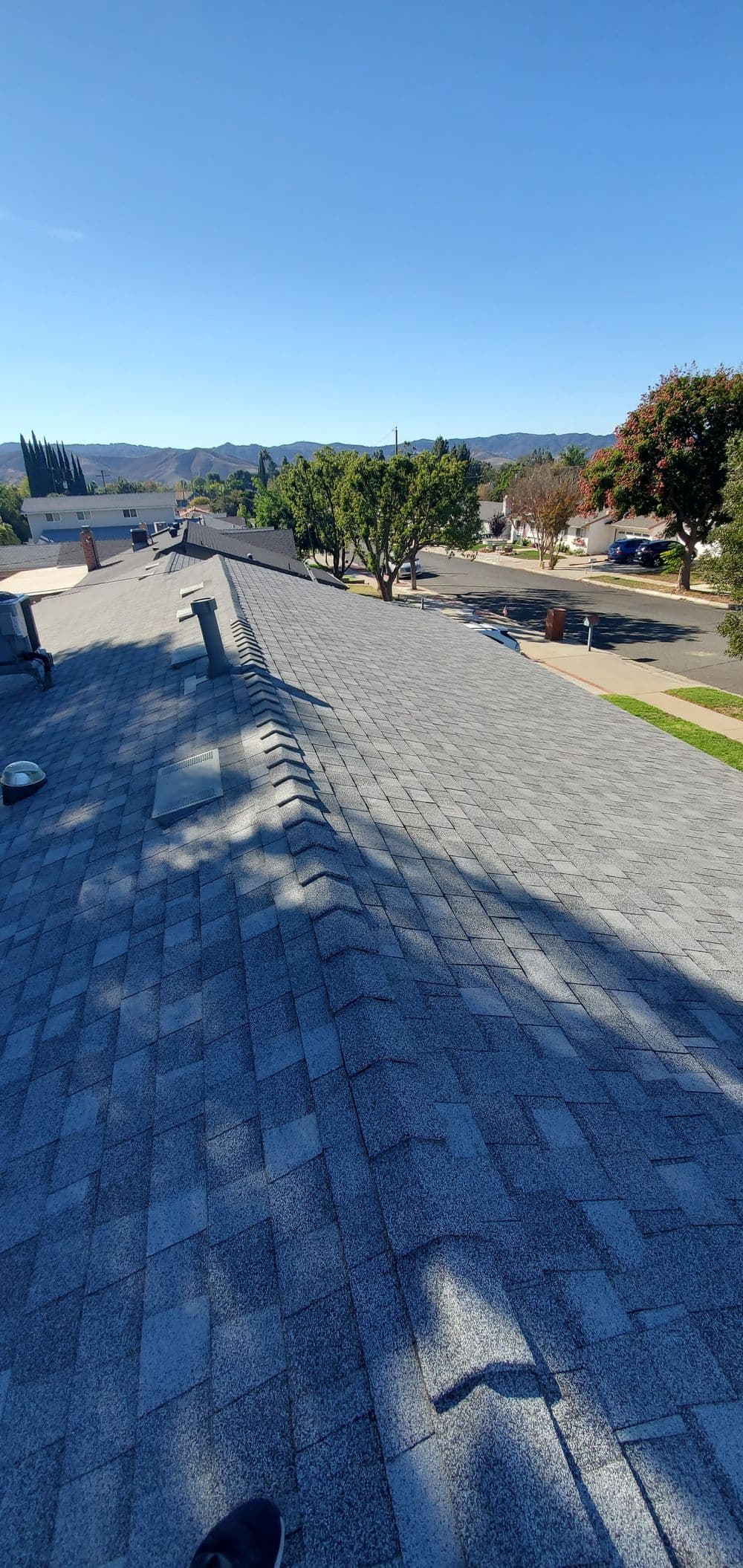 Gray shingle roof with a clear sky, trees, and a residential street in the background.