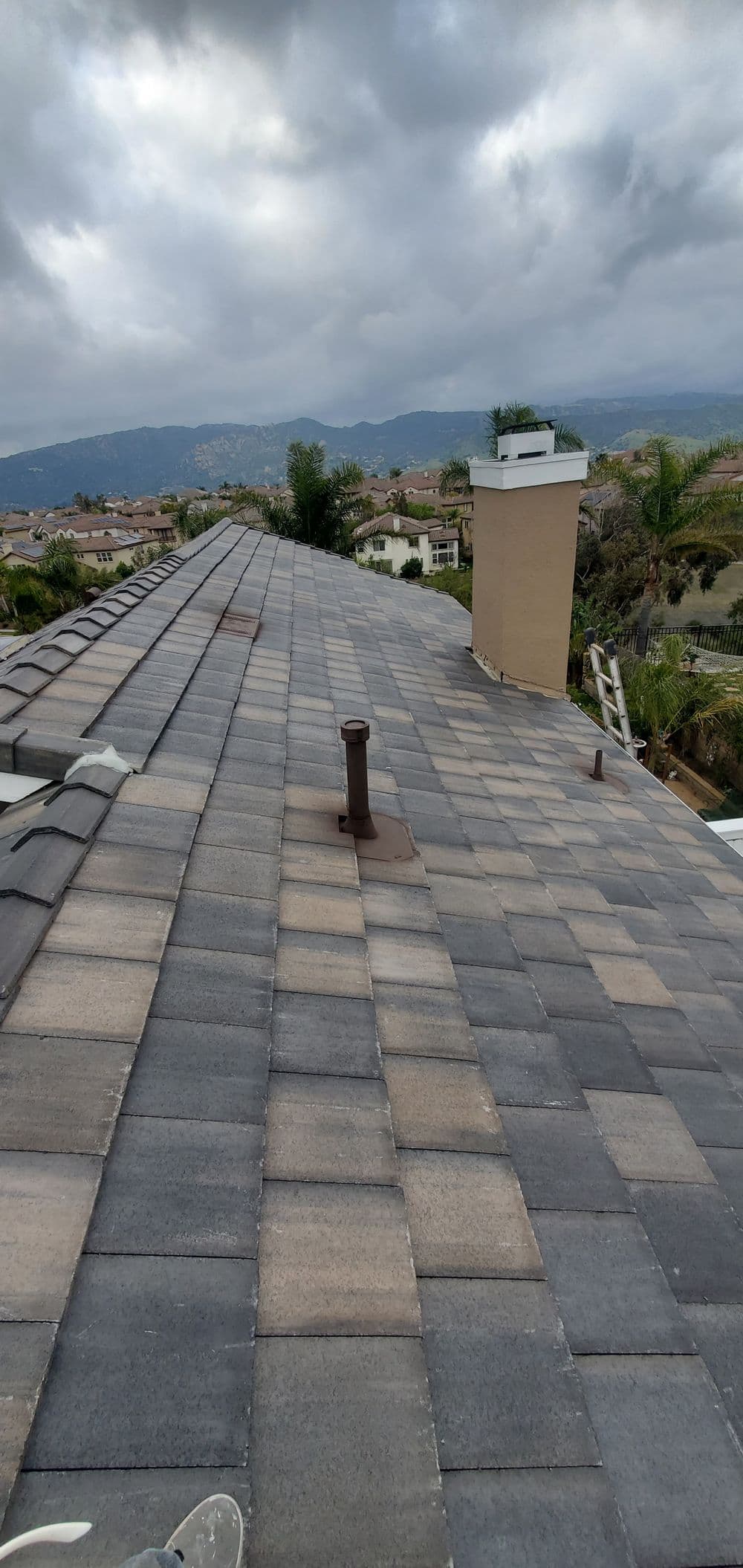 View of a residential roof with gray shingles and cloudy sky in the background, capturing landscape.