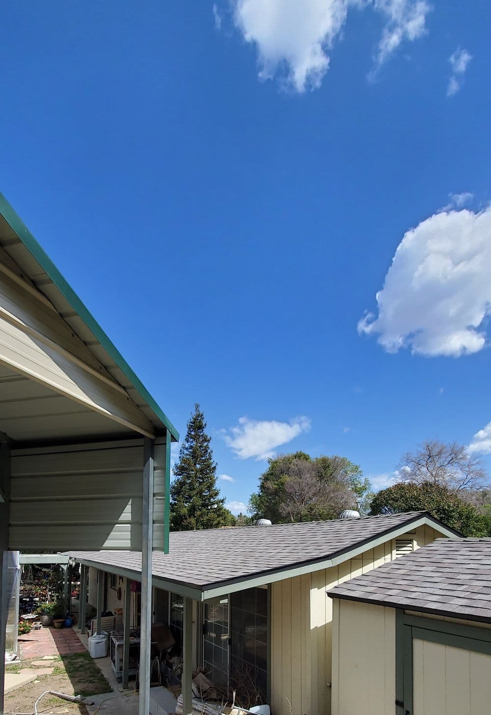 Clear blue sky with fluffy clouds above a residential building and green trees.