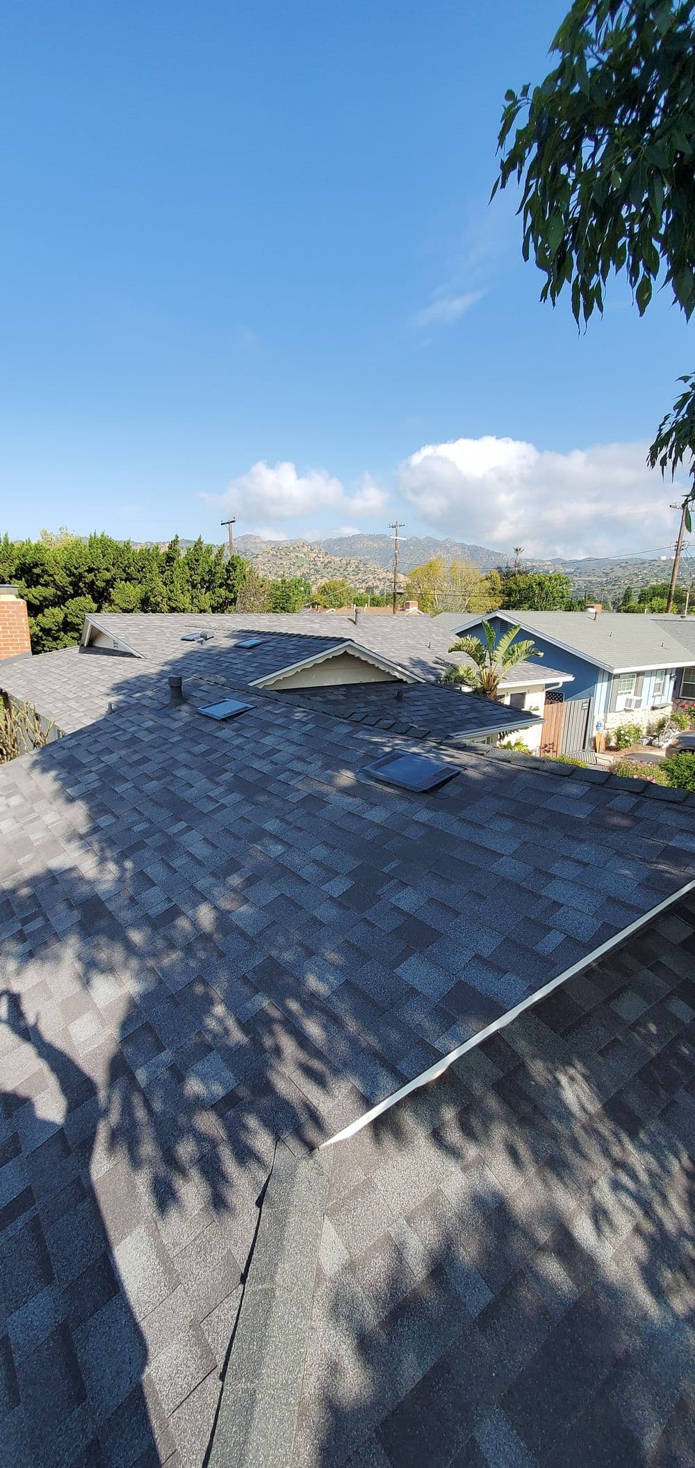 Aerial view of a modern shingle roof with skylights under a clear blue sky.