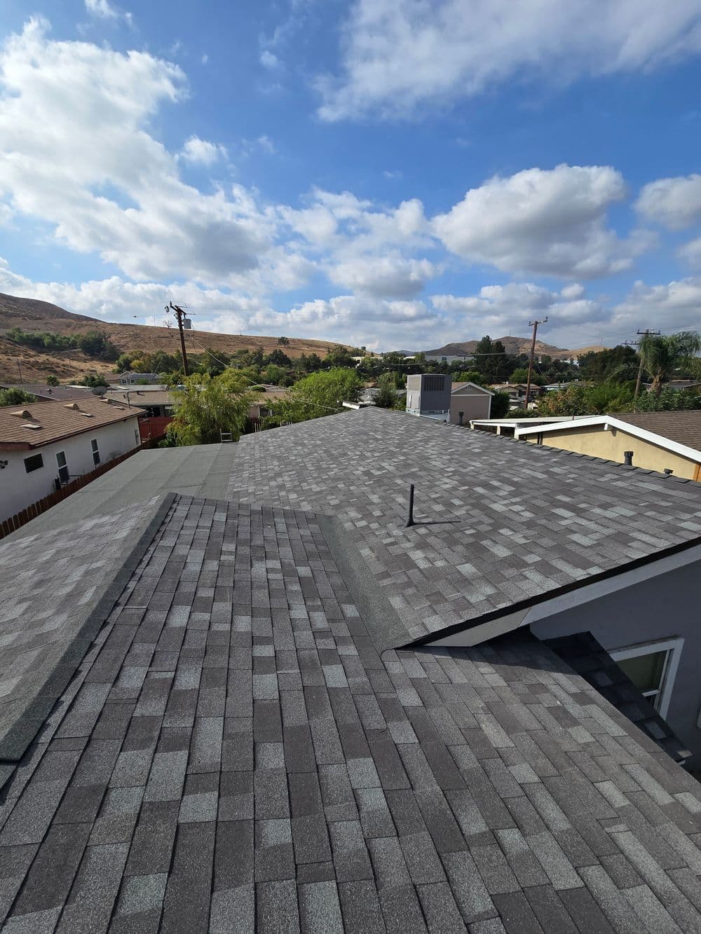 Aerial view of a newly shingled roof with blue sky and clouds in the background.