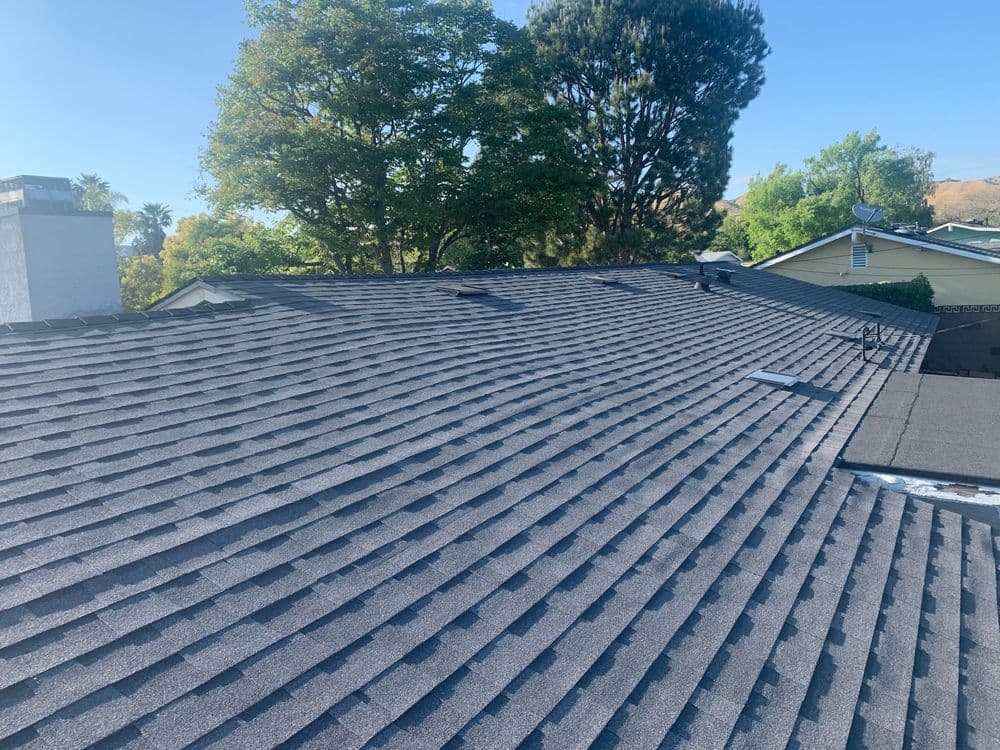 Newly installed gray asphalt shingle roof with skylights and lush green trees in the background.