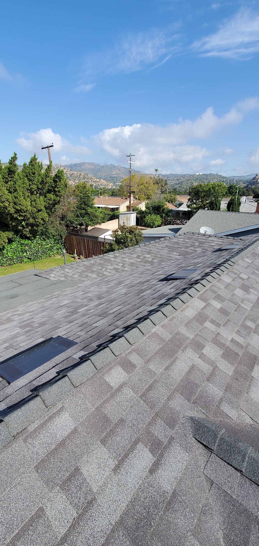 View of a residential roof with asphalt shingles and a clear blue sky in the background.