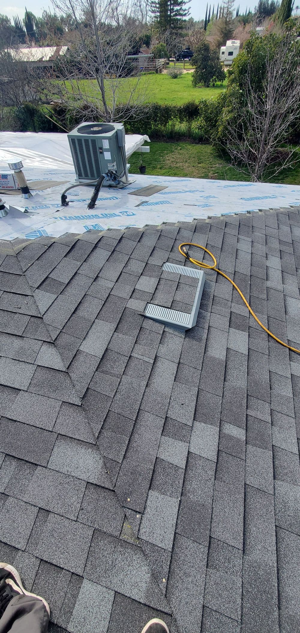 View of a sloped roof with shingles, an air conditioning unit, and installation tools.