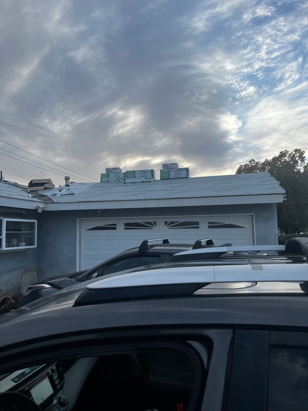 Roof with stacked materials and cloudy sky, viewed from a parked car.
