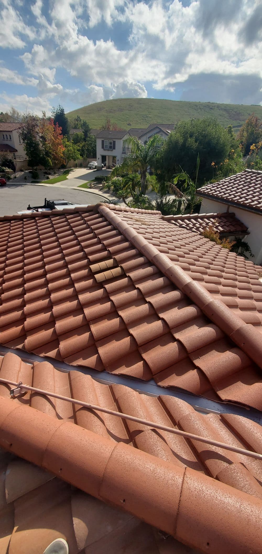 Red terracotta roof tiles with a scenic neighborhood and cloudy blue sky in the background.