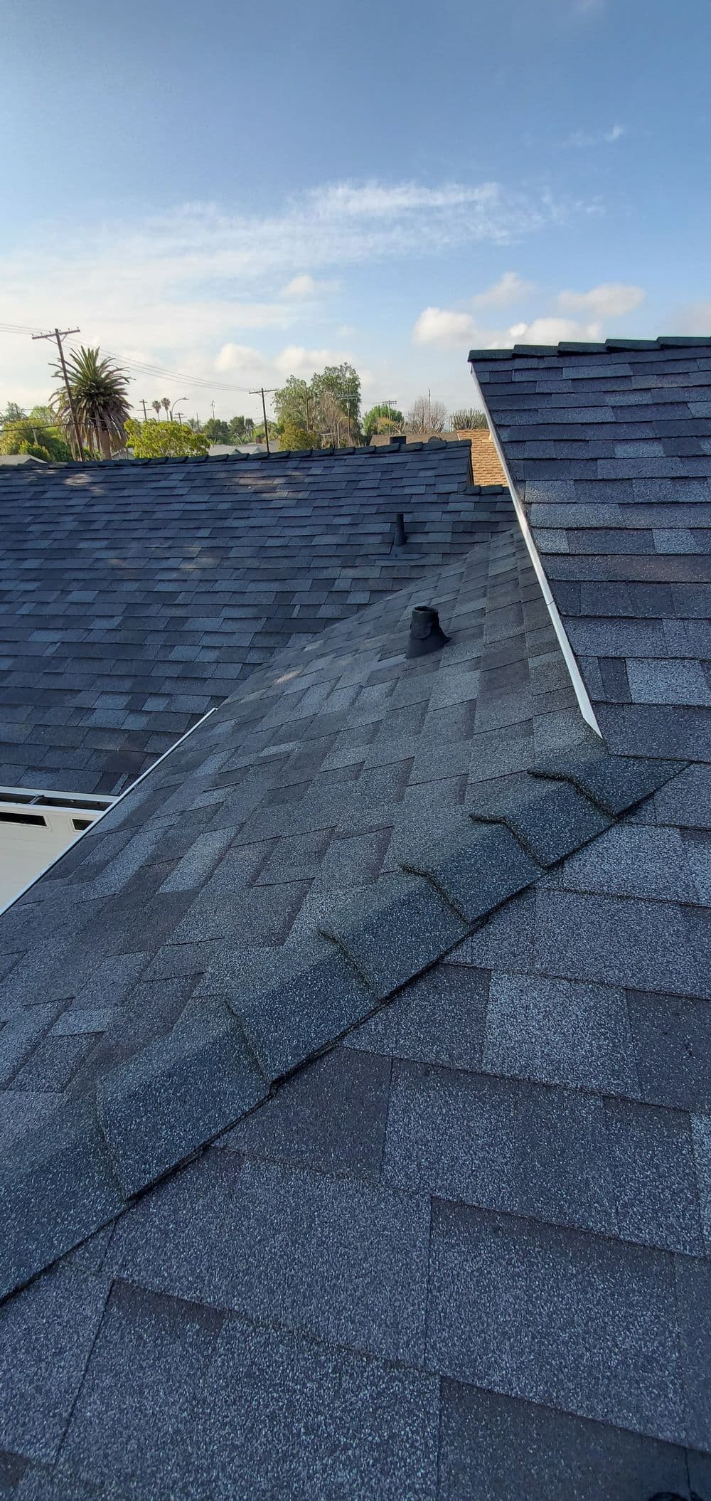 Roof shingles with vents under a clear blue sky, showcasing a residential property's exterior.