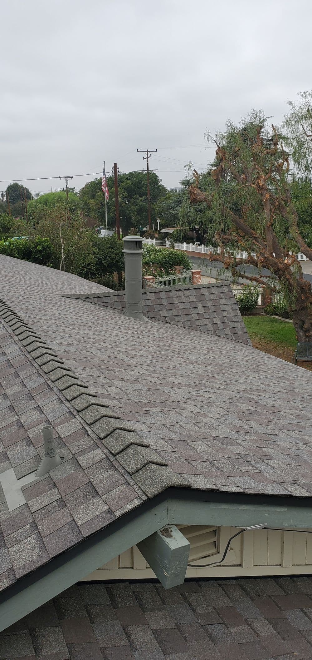 Aerial view of a shingle roof with a chimney and cloudy sky in the background.