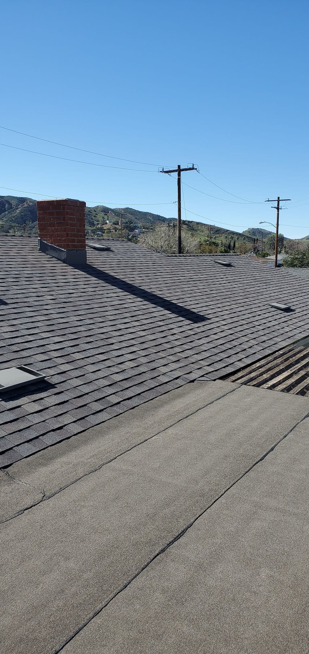 View of a sloped roof with chimney, skylights, and distant mountains under a clear blue sky.