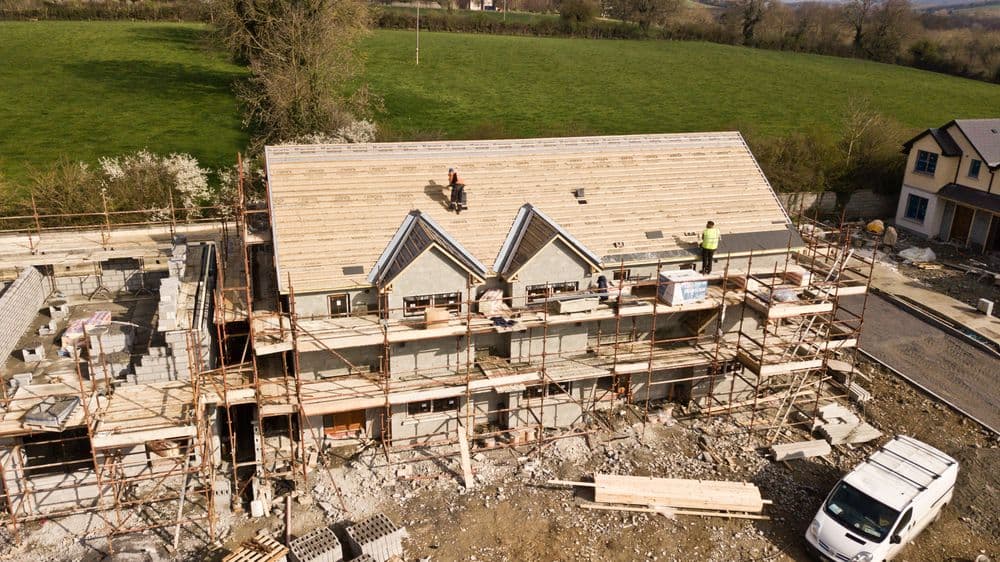Aerial view of a house under construction with scaffolding and workers on the roof.