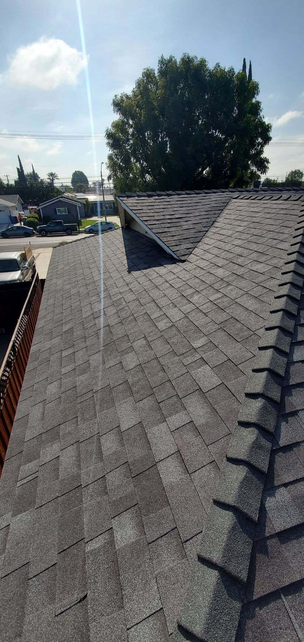 Newly installed asphalt shingle roof over a house with a clear blue sky in the background.