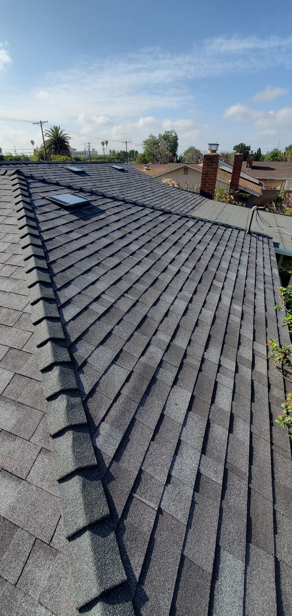 asphalt shingle roof with skylight and clear blue sky, showcasing roofing details and texture