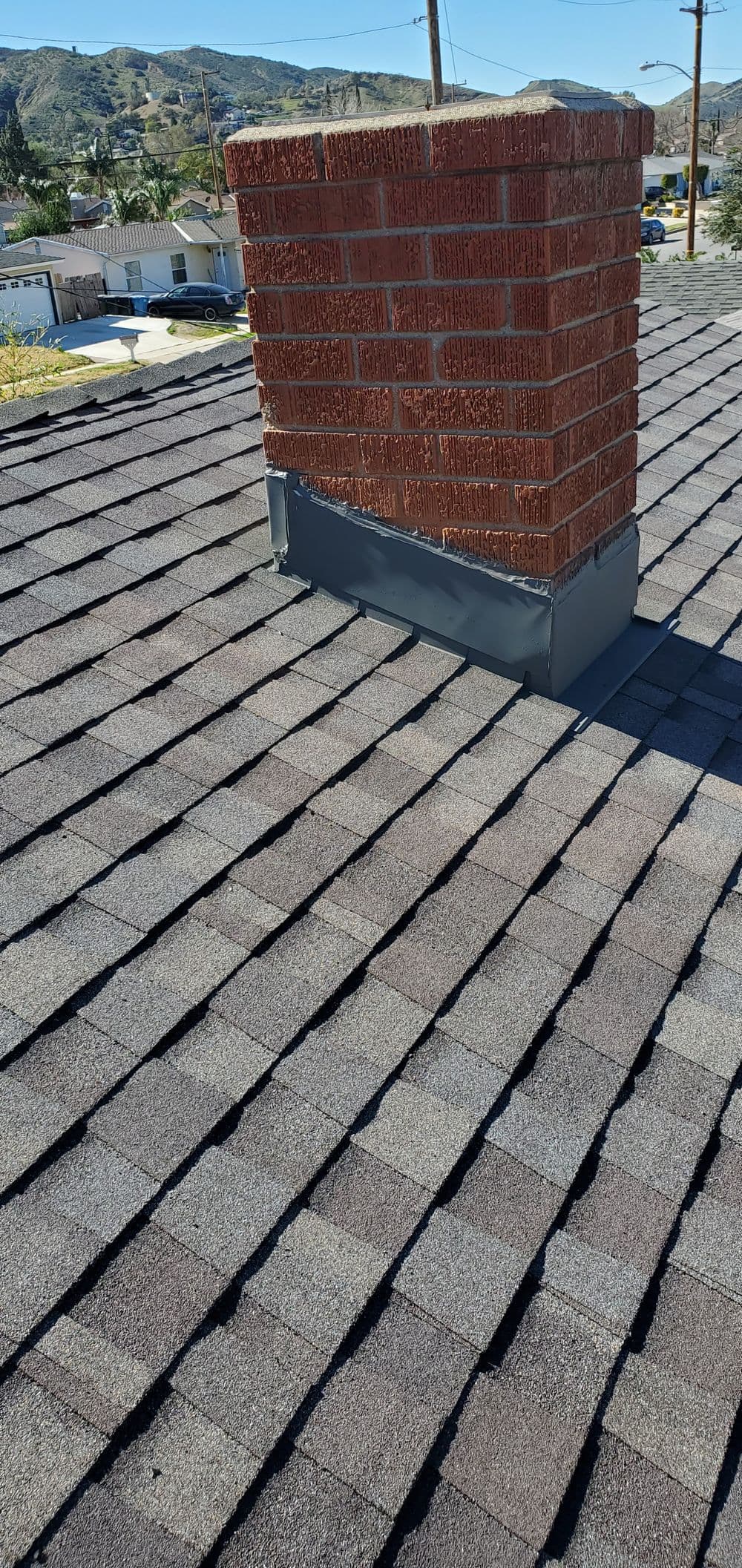 Chimney on a roof with asphalt shingles, showcasing an appealing landscape view in the background.