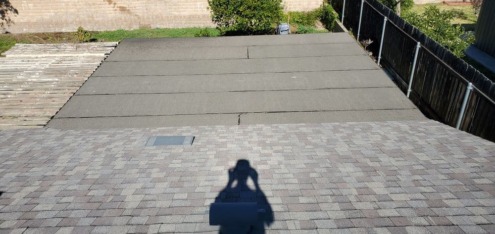 Roofing materials with a shadowed figure, showing a flat surface and nearby wooden deck.